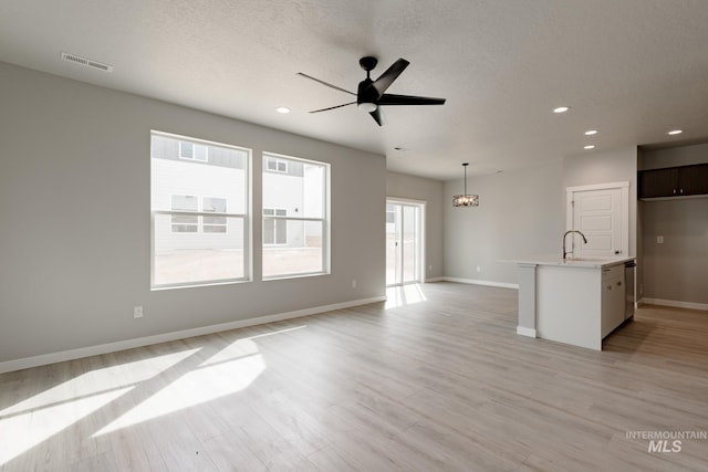 unfurnished living room with visible vents, baseboards, light wood-style flooring, a textured ceiling, and ceiling fan with notable chandelier