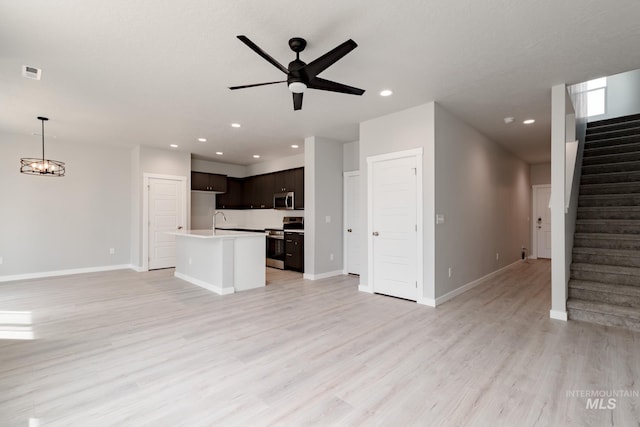 unfurnished living room featuring baseboards, light wood-style flooring, stairway, ceiling fan with notable chandelier, and recessed lighting