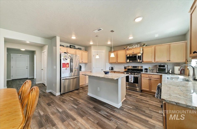 11299 W Taviton St, Nampa, ID 83651 - kitchen with appliances with stainless steel finishes, a sink, light brown cabinetry, dark wood finished floors, and a kitchen island