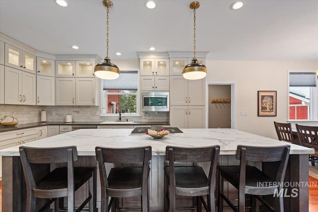 kitchen featuring dark stone counters, stainless steel appliances, decorative light fixtures, a kitchen island, and a breakfast bar area