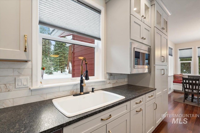 kitchen featuring decorative backsplash, stainless steel microwave, white cabinetry, and sink