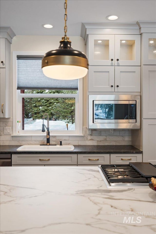 kitchen featuring white cabinetry, sink, light stone countertops, decorative light fixtures, and appliances with stainless steel finishes