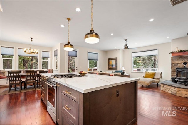 kitchen featuring a wood stove, ceiling fan with notable chandelier, high end stainless steel range oven, dark hardwood / wood-style floors, and light stone counters