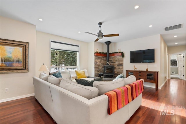 living room with dark hardwood / wood-style flooring, a wood stove, and ceiling fan