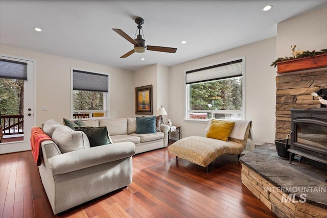 living room with dark hardwood / wood-style flooring, a wood stove, and ceiling fan