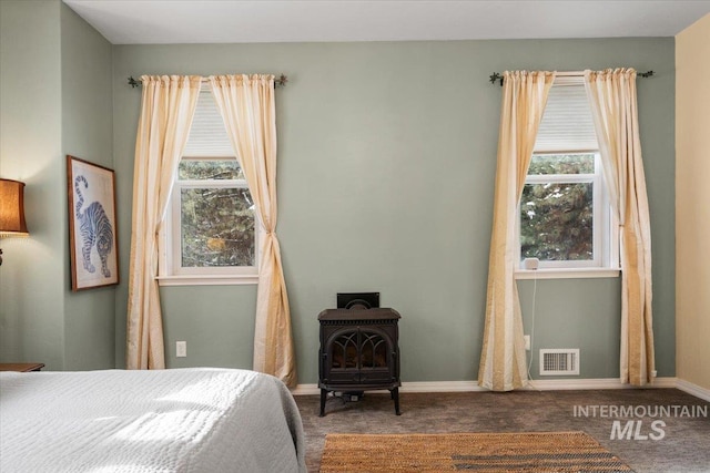 carpeted bedroom featuring a wood stove and multiple windows