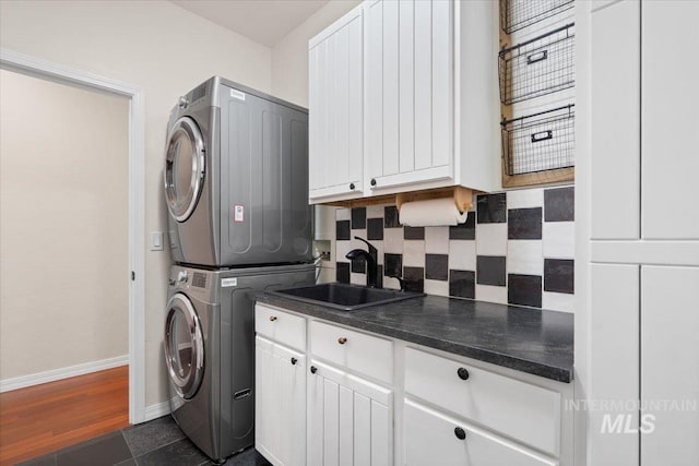 laundry room featuring dark tile patterned flooring, cabinets, stacked washer / dryer, and sink