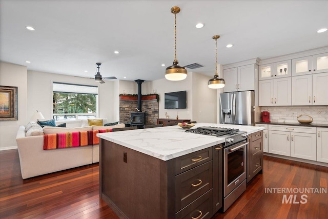 kitchen featuring a wood stove, hanging light fixtures, dark hardwood / wood-style floors, white cabinets, and appliances with stainless steel finishes