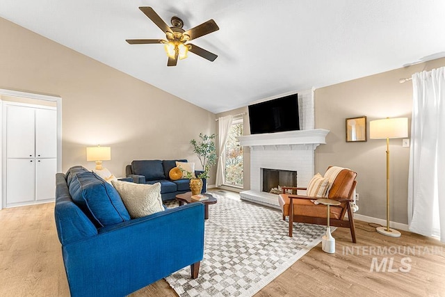 living area with lofted ceiling, ceiling fan, a fireplace, baseboards, and light wood-style floors