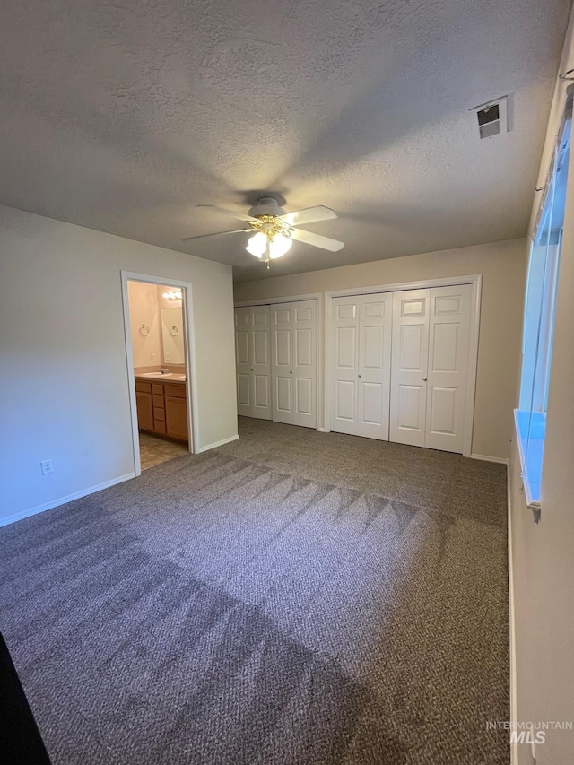 unfurnished bedroom featuring multiple closets, connected bathroom, ceiling fan, carpet, and a textured ceiling