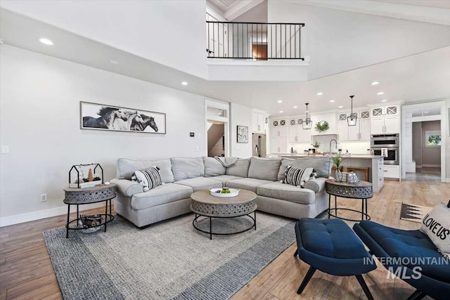 living room with sink, high vaulted ceiling, and light hardwood / wood-style flooring