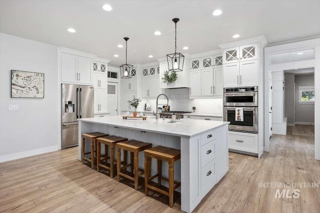 kitchen with stainless steel appliances, a breakfast bar, a center island with sink, and white cabinets