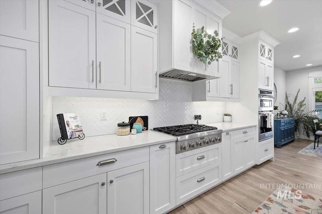 kitchen with appliances with stainless steel finishes, tasteful backsplash, white cabinets, light stone countertops, and light wood-type flooring