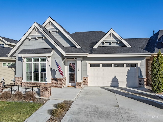 craftsman inspired home featuring driveway, an attached garage, roof with shingles, and brick siding