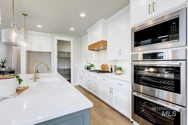 kitchen featuring appliances with stainless steel finishes, a sink, light wood-style floors, recessed lighting, and backsplash