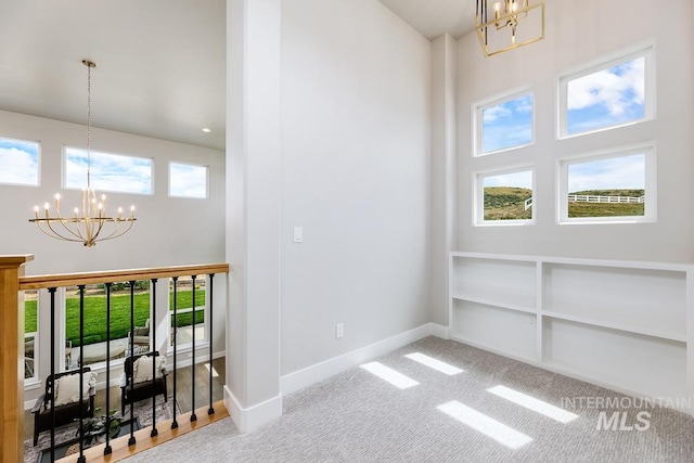 carpeted empty room featuring baseboards, a chandelier, and a towering ceiling