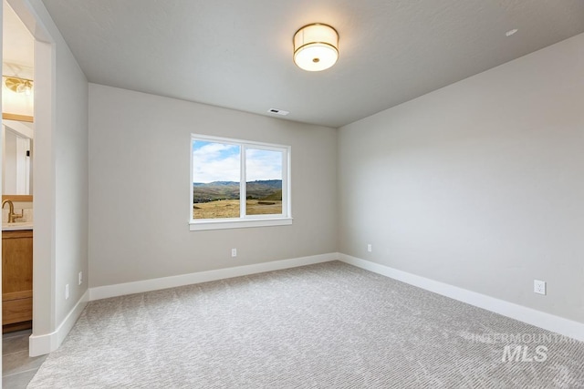 spare room featuring light colored carpet, a sink, baseboards, and visible vents