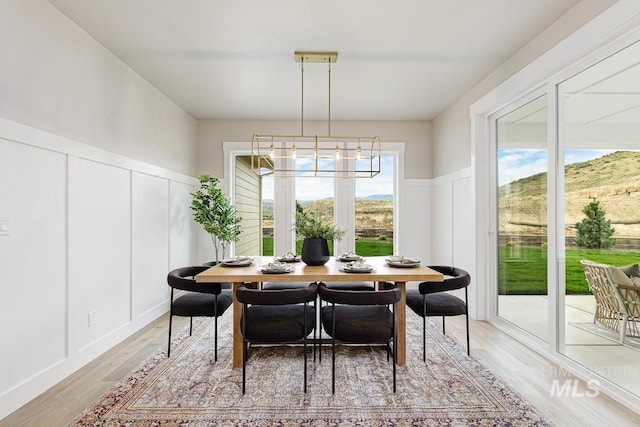 dining area with wainscoting, a decorative wall, light wood finished floors, and a notable chandelier