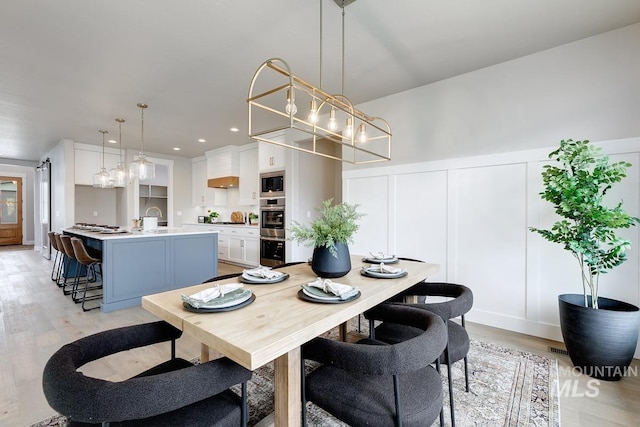 dining space with a decorative wall, light wood-type flooring, recessed lighting, a wainscoted wall, and a notable chandelier