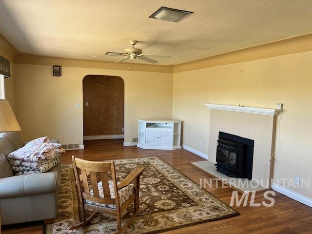 living area featuring baseboards, a wood stove, visible vents, ceiling fan, and arched walkways