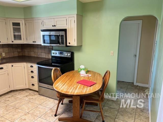 kitchen featuring light tile patterned floors, arched walkways, appliances with stainless steel finishes, dark countertops, and backsplash