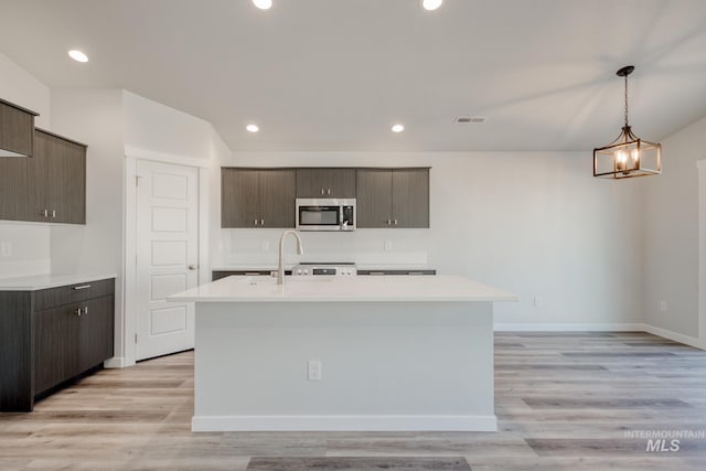 7308 E Marble Springs Dr, Nampa, ID 83687 - kitchen with dark brown cabinetry, a kitchen island with sink, stainless steel microwave, light countertops, and visible vents