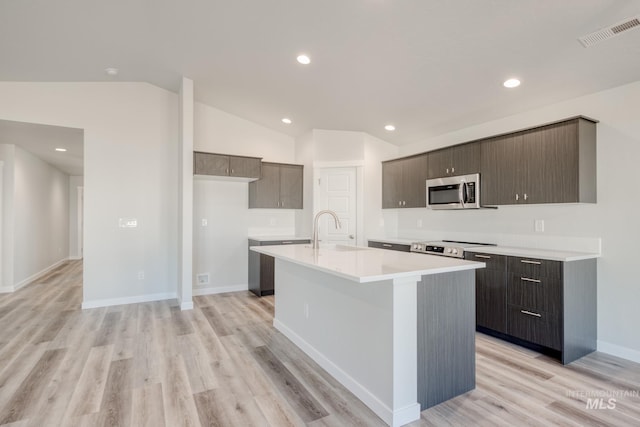 7308 E Marble Springs Dr, Nampa, ID 83687 - kitchen with stainless steel microwave, light countertops, light wood-type flooring, vaulted ceiling, and a center island with sink