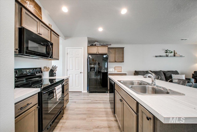 kitchen with open floor plan, light countertops, light wood-style flooring, black appliances, and a sink