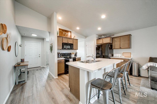 kitchen featuring lofted ceiling, a sink, black appliances, light countertops, and a kitchen bar