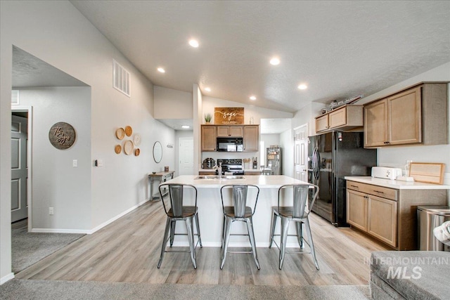 kitchen with a sink, lofted ceiling, black appliances, and a breakfast bar