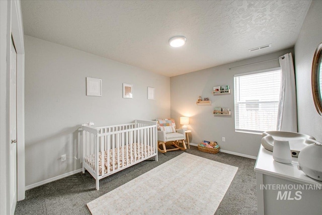 carpeted bedroom with a crib, baseboards, visible vents, and a textured ceiling