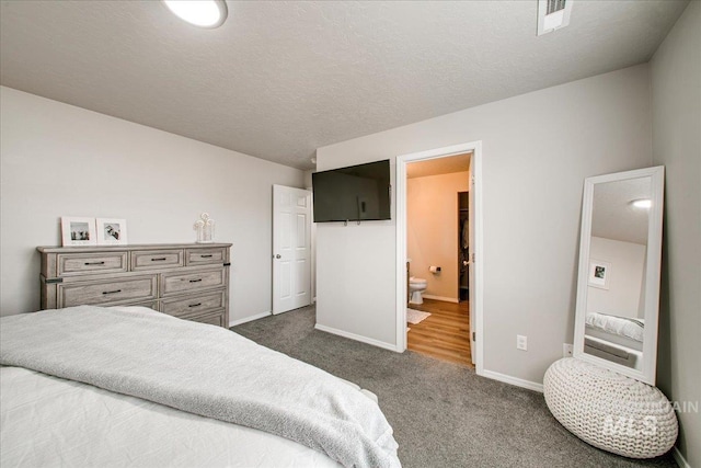 bedroom featuring visible vents, a textured ceiling, ensuite bath, dark carpet, and baseboards