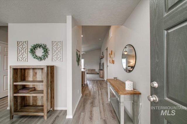 foyer featuring light wood-style flooring, a textured ceiling, and baseboards