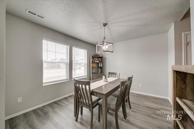 dining space with a notable chandelier, visible vents, a textured ceiling, and light wood-type flooring