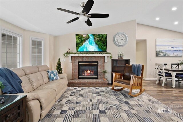 living area featuring baseboards, lofted ceiling, wood finished floors, a brick fireplace, and recessed lighting