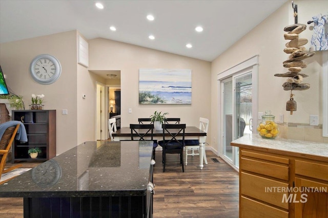 interior space featuring dark wood finished floors, a kitchen island, vaulted ceiling, and dark stone countertops