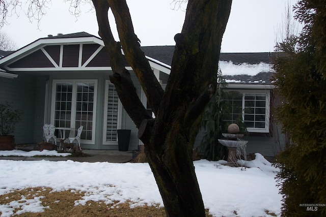 snow covered property featuring roof with shingles