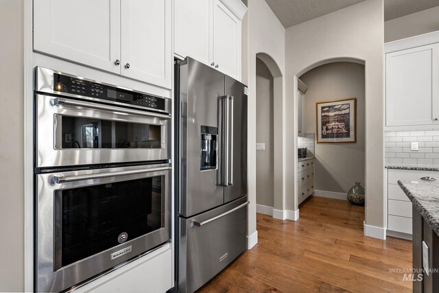 1102 N Longhorn Ave, Eagle, ID 83616 - kitchen featuring white cabinets, dark wood finished floors, decorative backsplash, light stone countertops, and stainless steel appliances