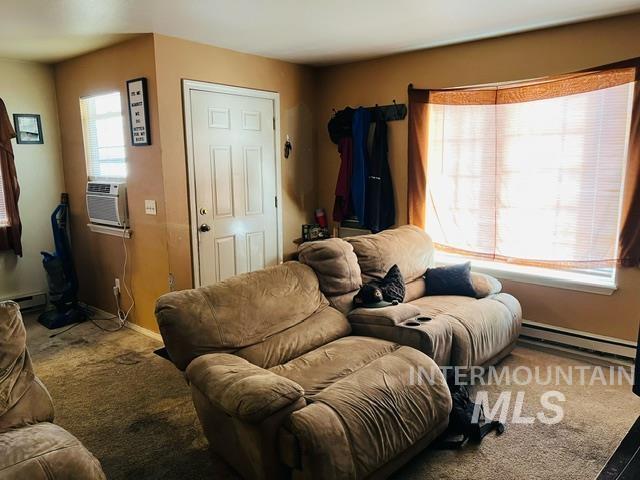 carpeted living area featuring a baseboard heating unit, cooling unit, and plenty of natural light