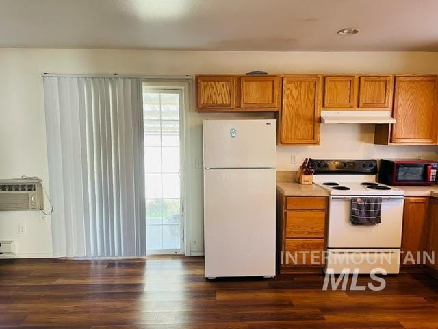 kitchen featuring dark wood-type flooring, under cabinet range hood, a wall unit AC, brown cabinets, and white appliances