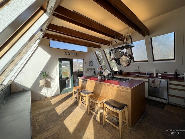 kitchen with beam ceiling, a sink, dark countertops, a kitchen island, and appliances with stainless steel finishes