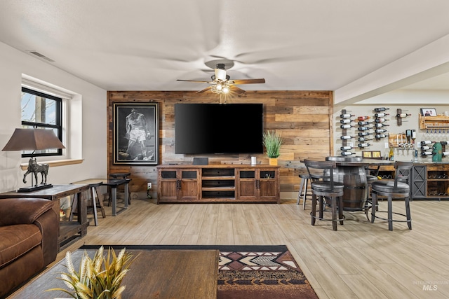 living room featuring ceiling fan, bar area, light wood-type flooring, and wood walls