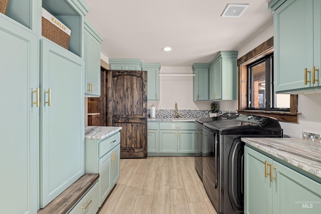 laundry area featuring cabinets, sink, washing machine and dryer, and light hardwood / wood-style flooring