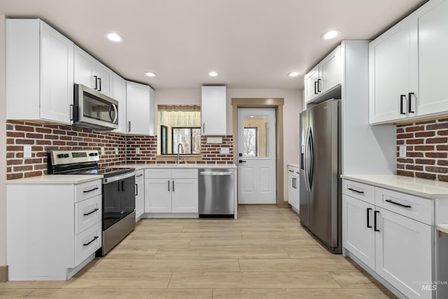 kitchen with sink, tasteful backsplash, light wood-type flooring, appliances with stainless steel finishes, and white cabinets