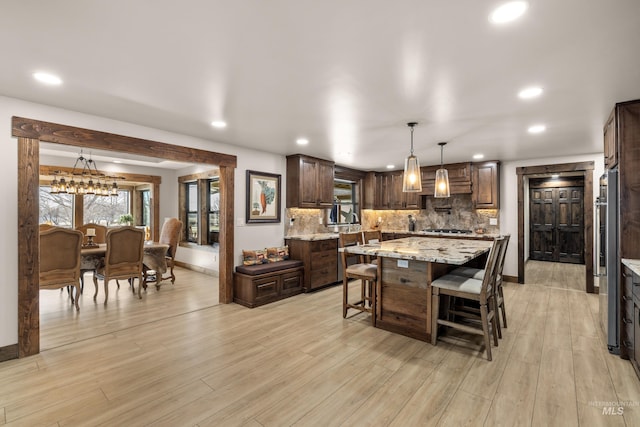 kitchen featuring backsplash, hanging light fixtures, a center island, light stone counters, and light hardwood / wood-style floors