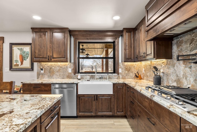 kitchen featuring appliances with stainless steel finishes, sink, custom exhaust hood, light stone counters, and dark brown cabinets