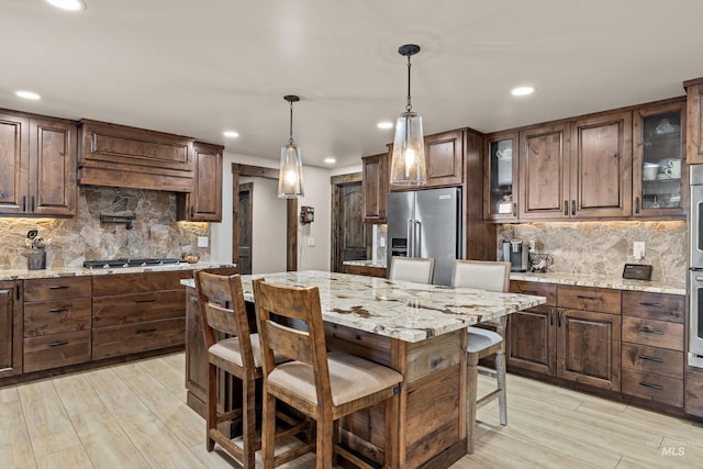 kitchen featuring a breakfast bar, appliances with stainless steel finishes, a center island, light stone countertops, and decorative light fixtures