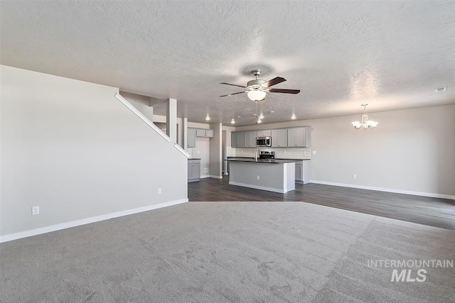 unfurnished living room with dark carpet, sink, ceiling fan with notable chandelier, and a textured ceiling