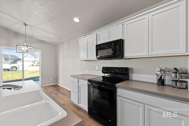 kitchen featuring sink, a notable chandelier, lofted ceiling, white cabinets, and black appliances