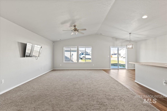 unfurnished living room featuring a textured ceiling, vaulted ceiling, a healthy amount of sunlight, and ceiling fan with notable chandelier